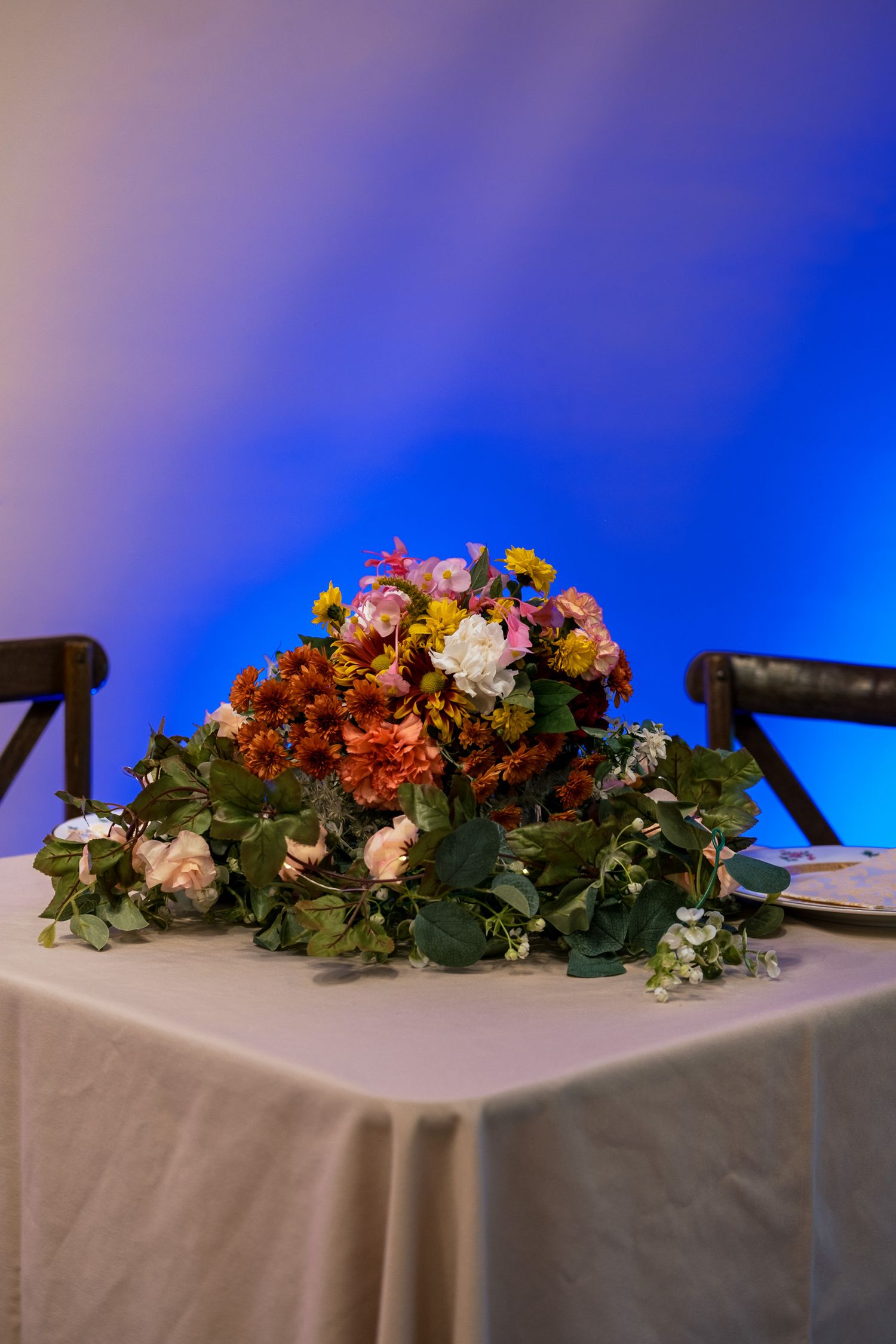 Colorful floral centerpiece with orange, pink, and white blooms on a white tablecloth.
