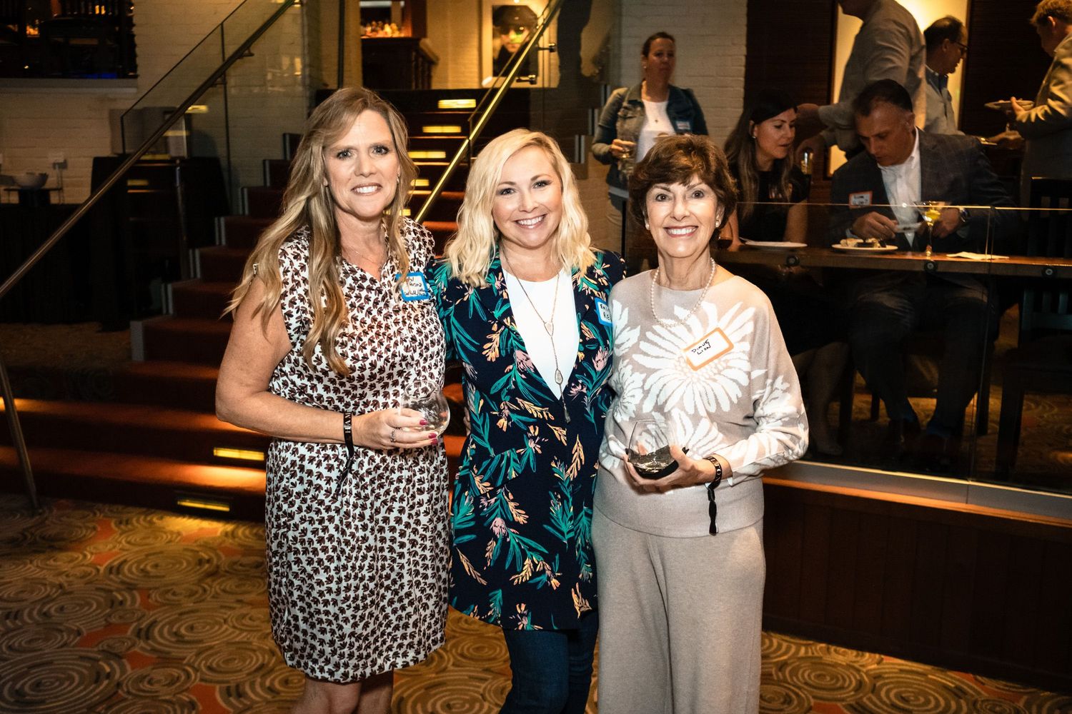 Three women smiling and holding crystal awards at an elegant indoor event celebration.