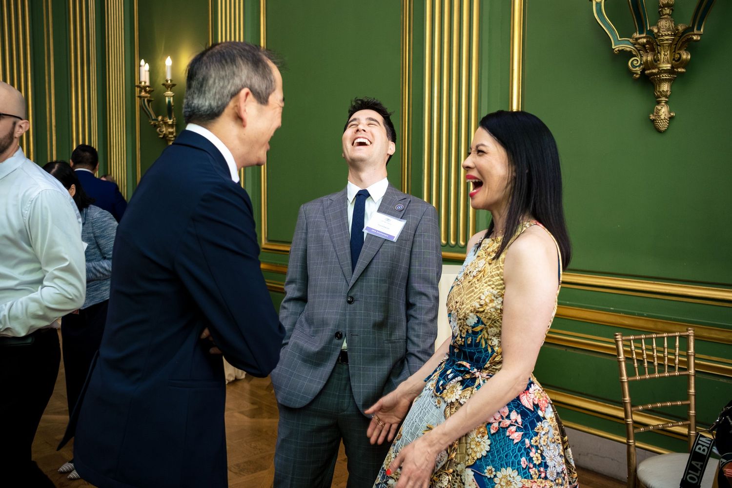 Three people laughing together at an elegant green-walled formal event venue.