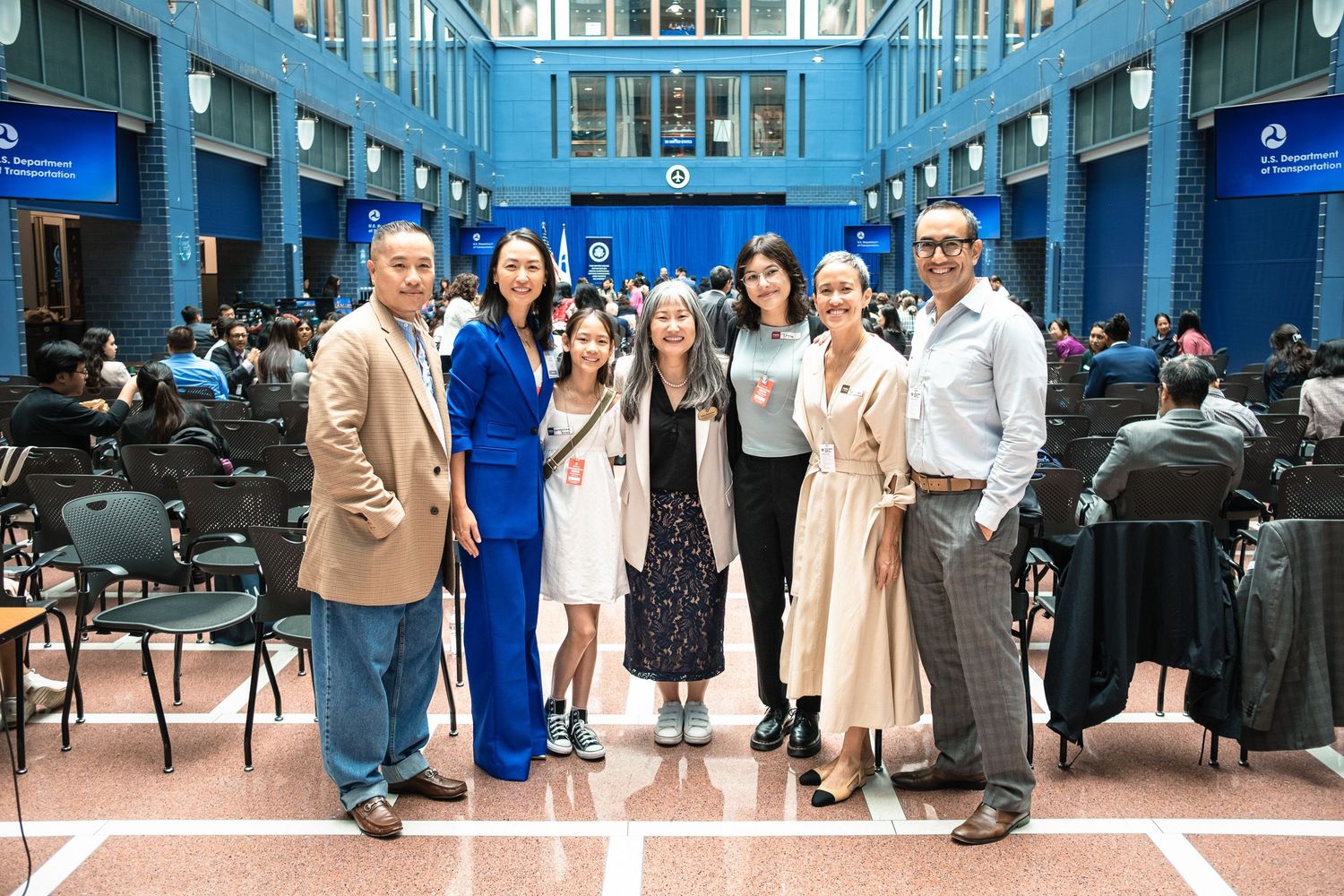 Group of seven people pose together smiling in a blue atrium at a formal graduation event.