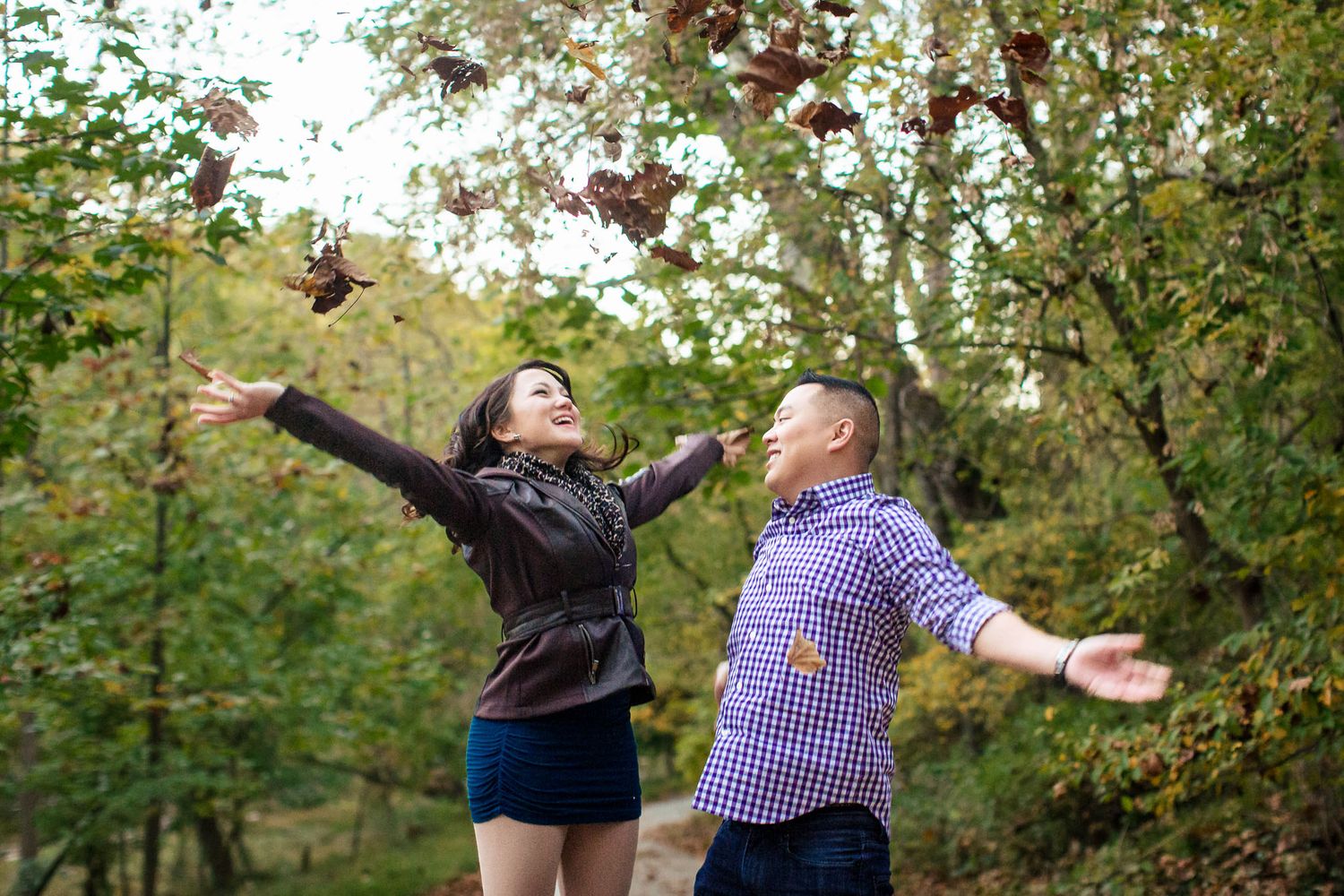 Couple joyfully tossing autumn leaves in the air in a colorful fall forest.