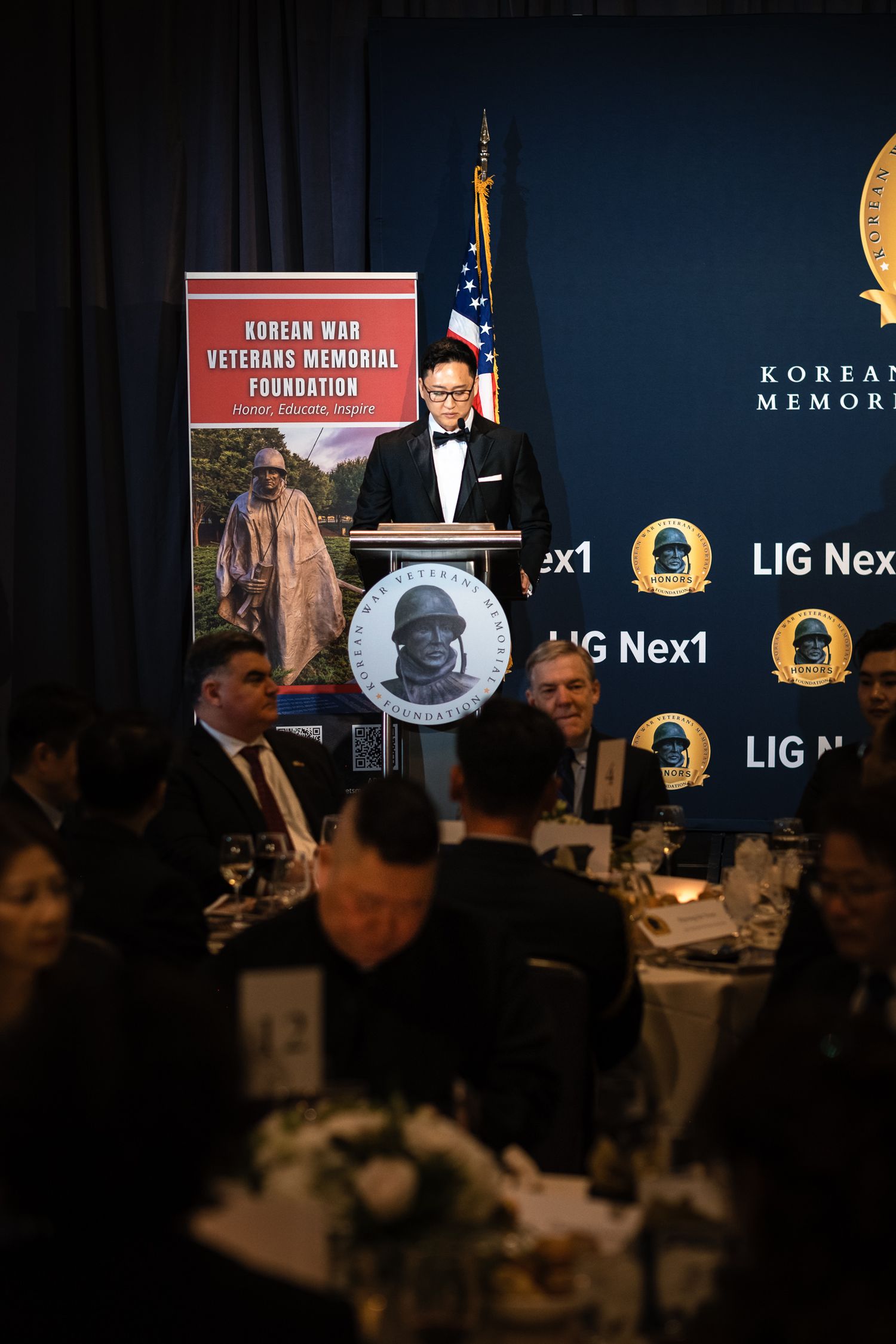 Speaker at Korean War Veterans Memorial Foundation gala podium with LIG Nex1 sponsor backdrop.