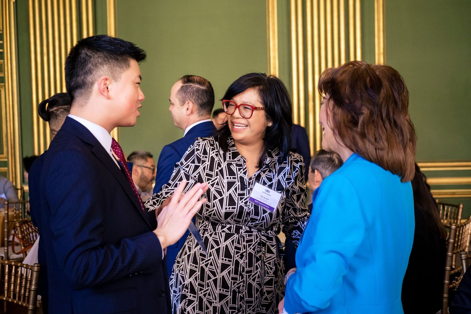 Professionals networking at a formal event in an elegant green-walled venue, engaged in conversation.