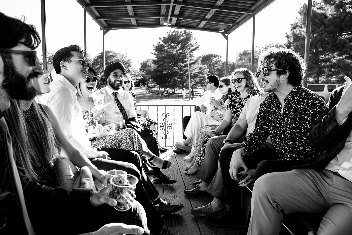 Black and white photo of wedding guests socializing under a pavilion at an outdoor reception.