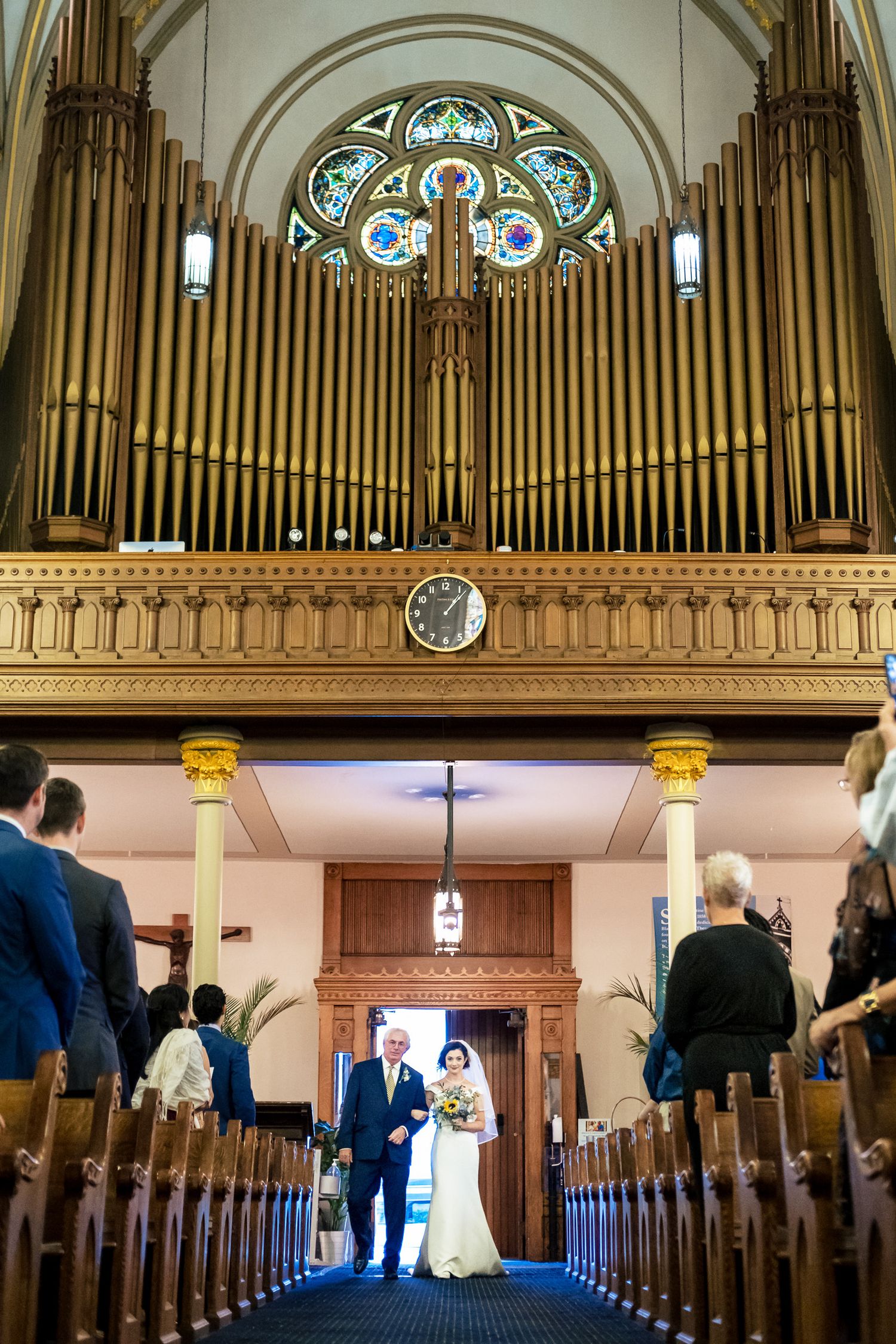 Bride walks down the aisle with escort beneath a grand pipe organ in an elegant church wedding.