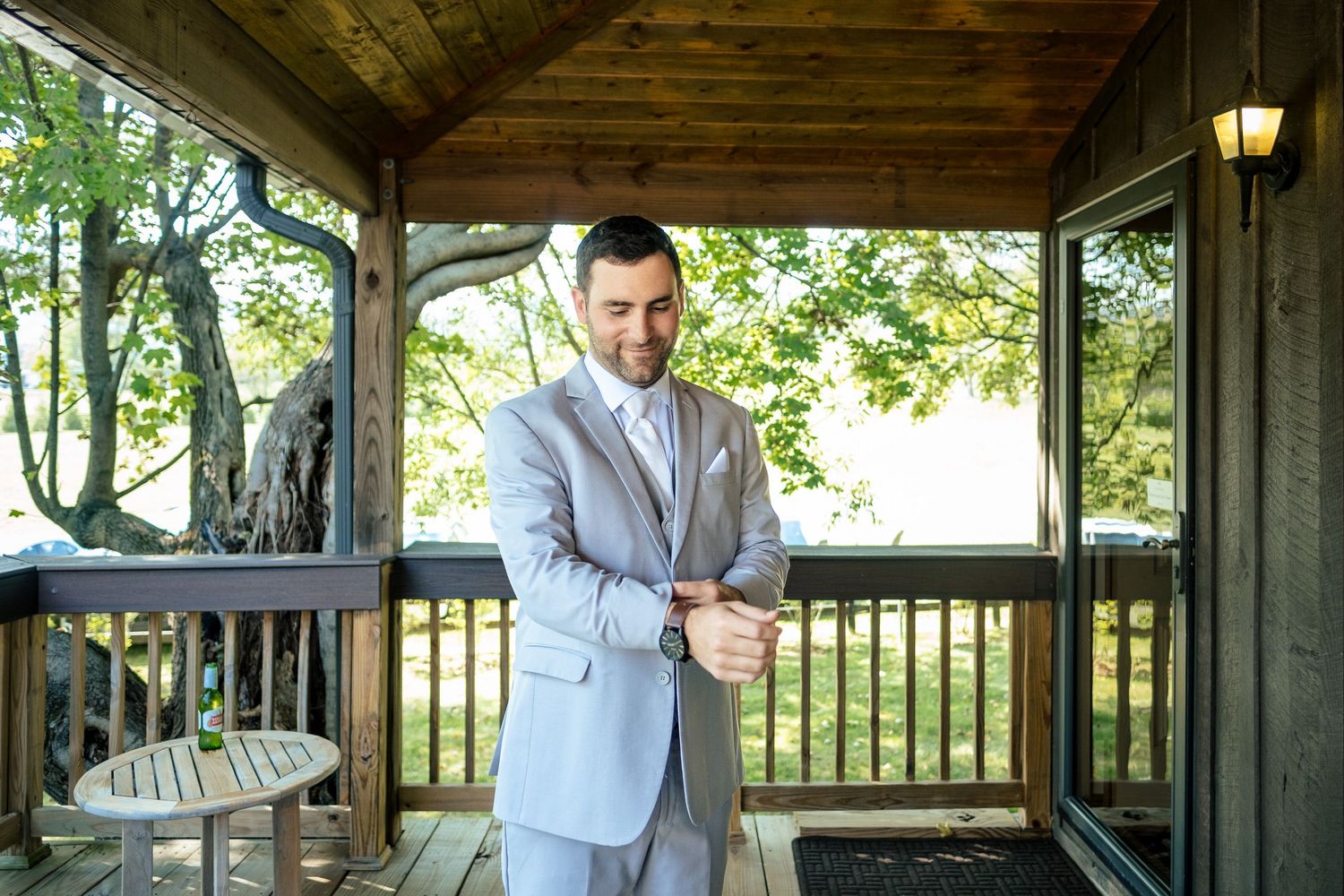Handsome groom in light gray suit checking his watch on a wooden deck before the wedding.