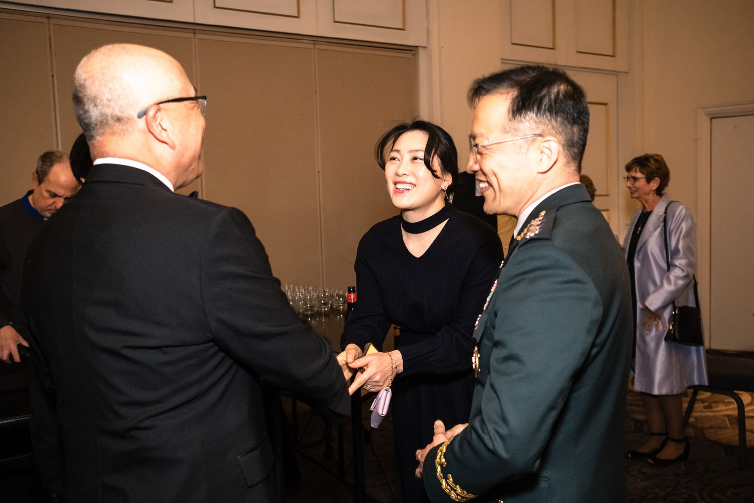 Military officer in uniform shakes hands with guests at a formal reception event.