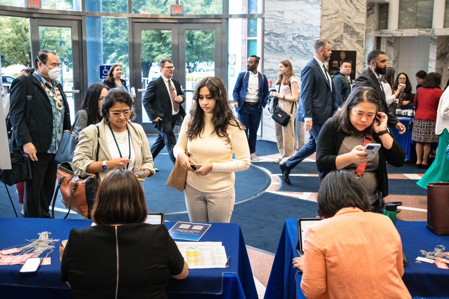 Attendees check in at registration tables during a busy professional conference in a modern venue.