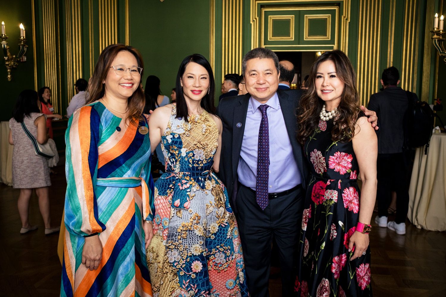 Four elegantly dressed guests smile together at a formal event in a green-walled ballroom.