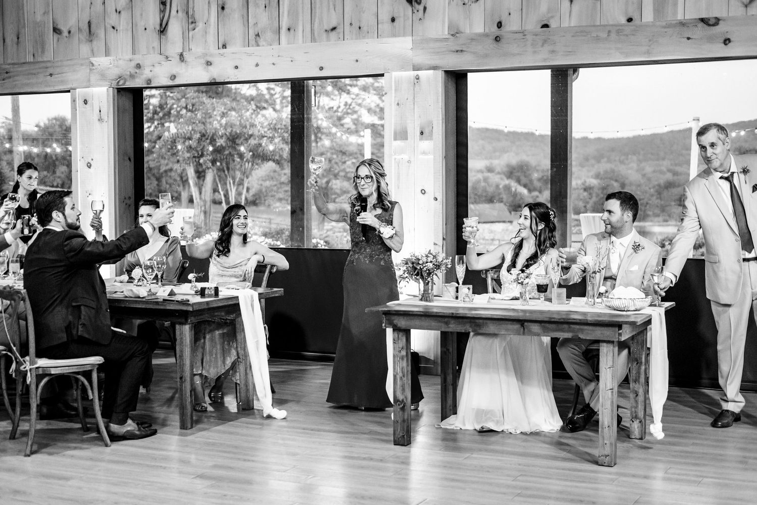 Black and white photo of bridesmaid giving toast at wedding reception in rustic barn venue.