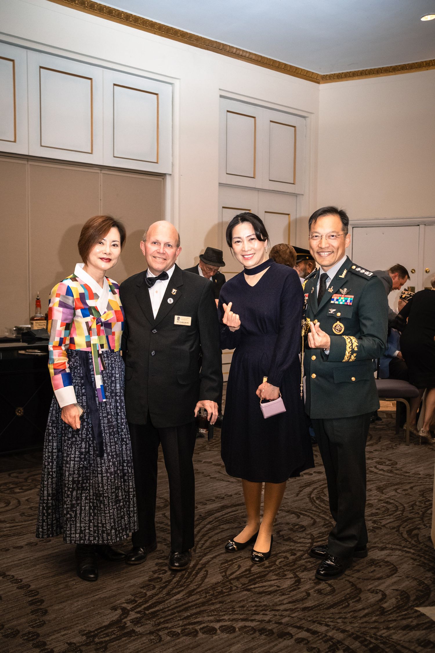 Four elegantly dressed guests pose together at a formal event, including a woman in hanbok and a man in military uniform.