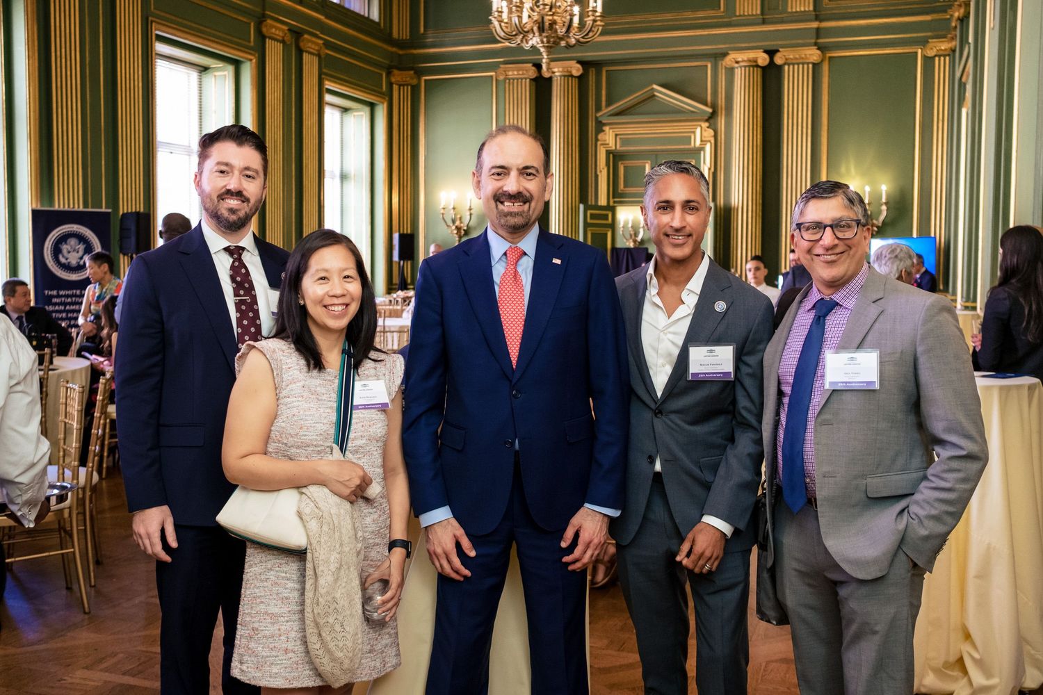 Five professionals pose together smiling at an elegant formal event in a ornate green ballroom.