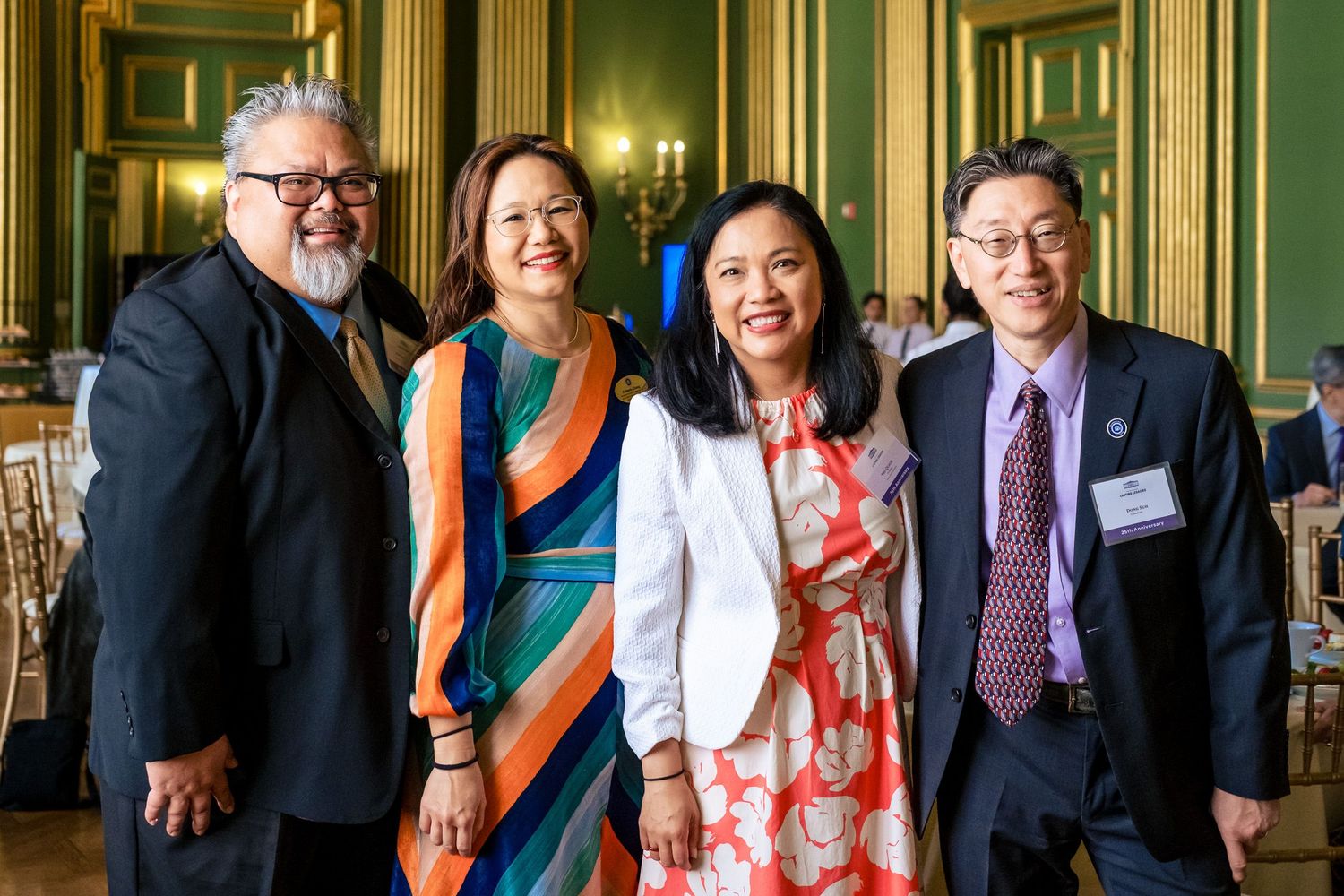 Four Asian professionals smile together at an elegant green-walled formal reception event.