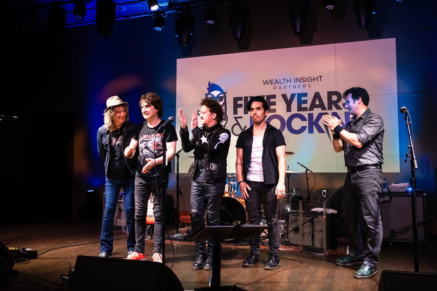 Five performers on stage at Wealth Insight Five Years Rock anniversary event under colorful lighting.
