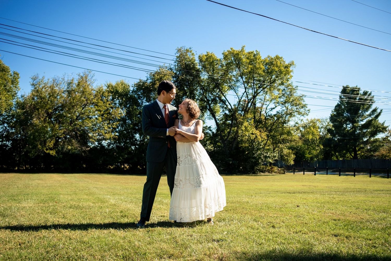 Bride and groom sharing a tender moment together on a wide green lawn under a clear blue sky.