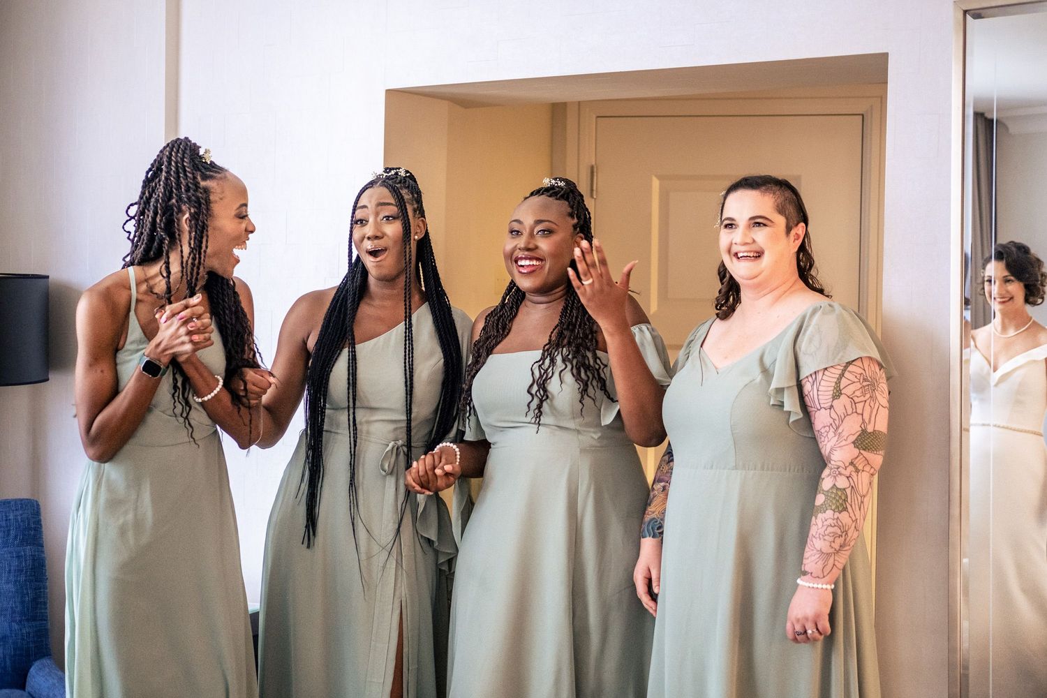 Four bridesmaids in sage green dresses laugh and react emotionally during bridal first look reveal.