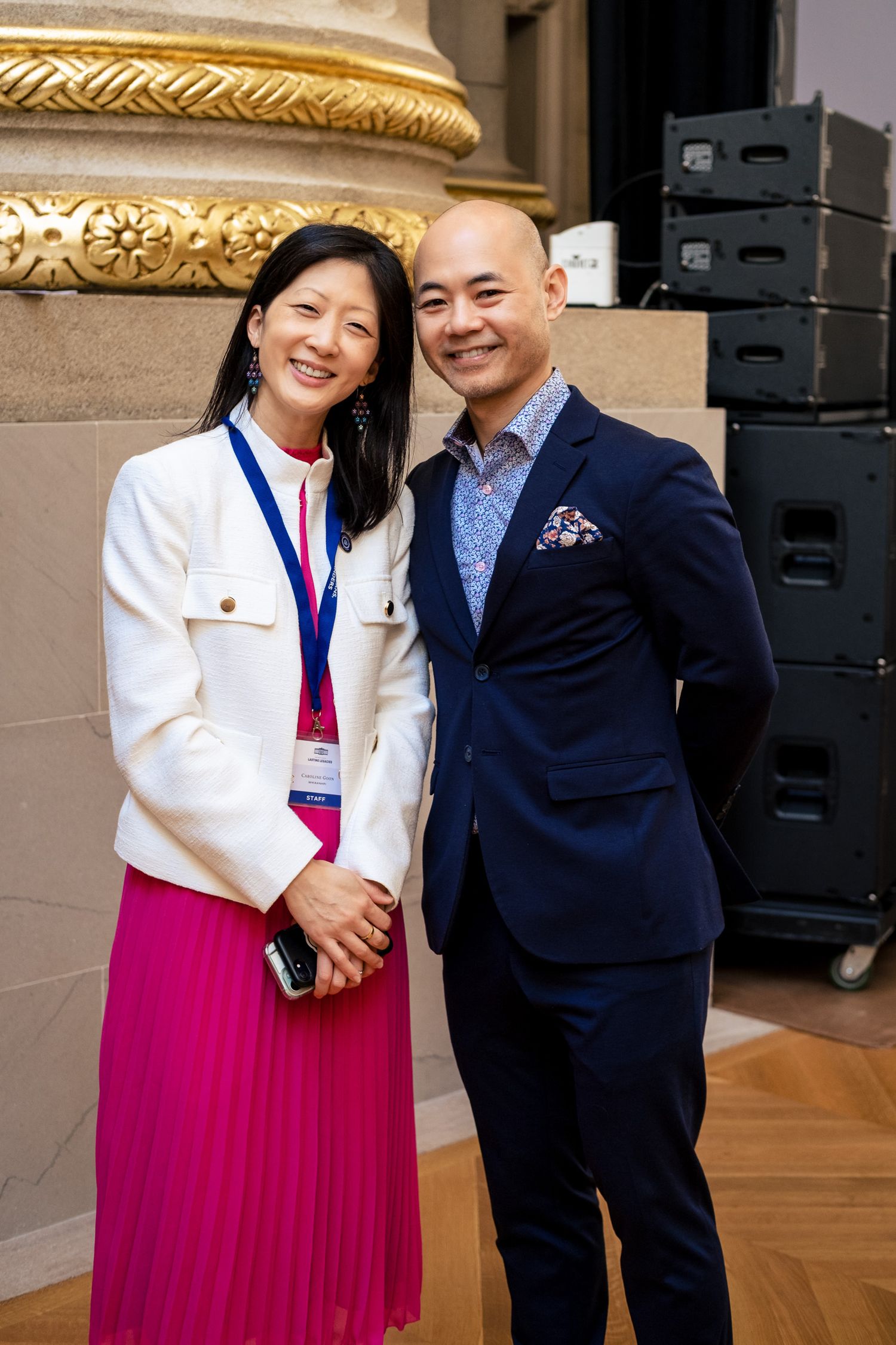 A smiling man and woman in formal attire pose together at an elegant event venue.
