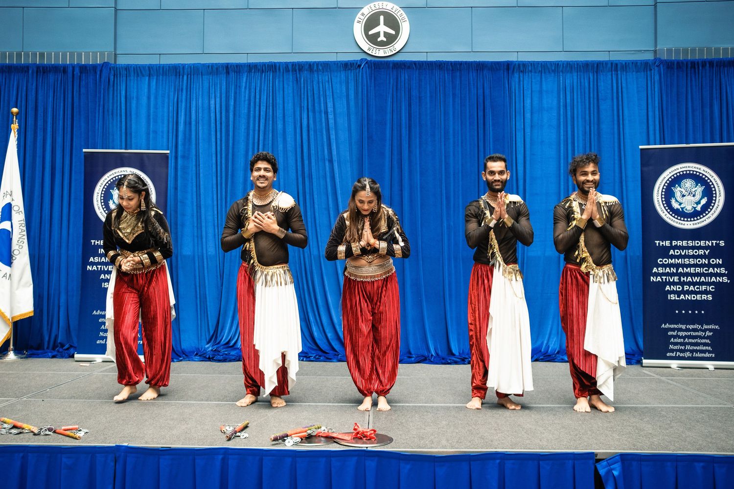 Five performers in traditional red and white costumes bow on stage at a cultural dance event.