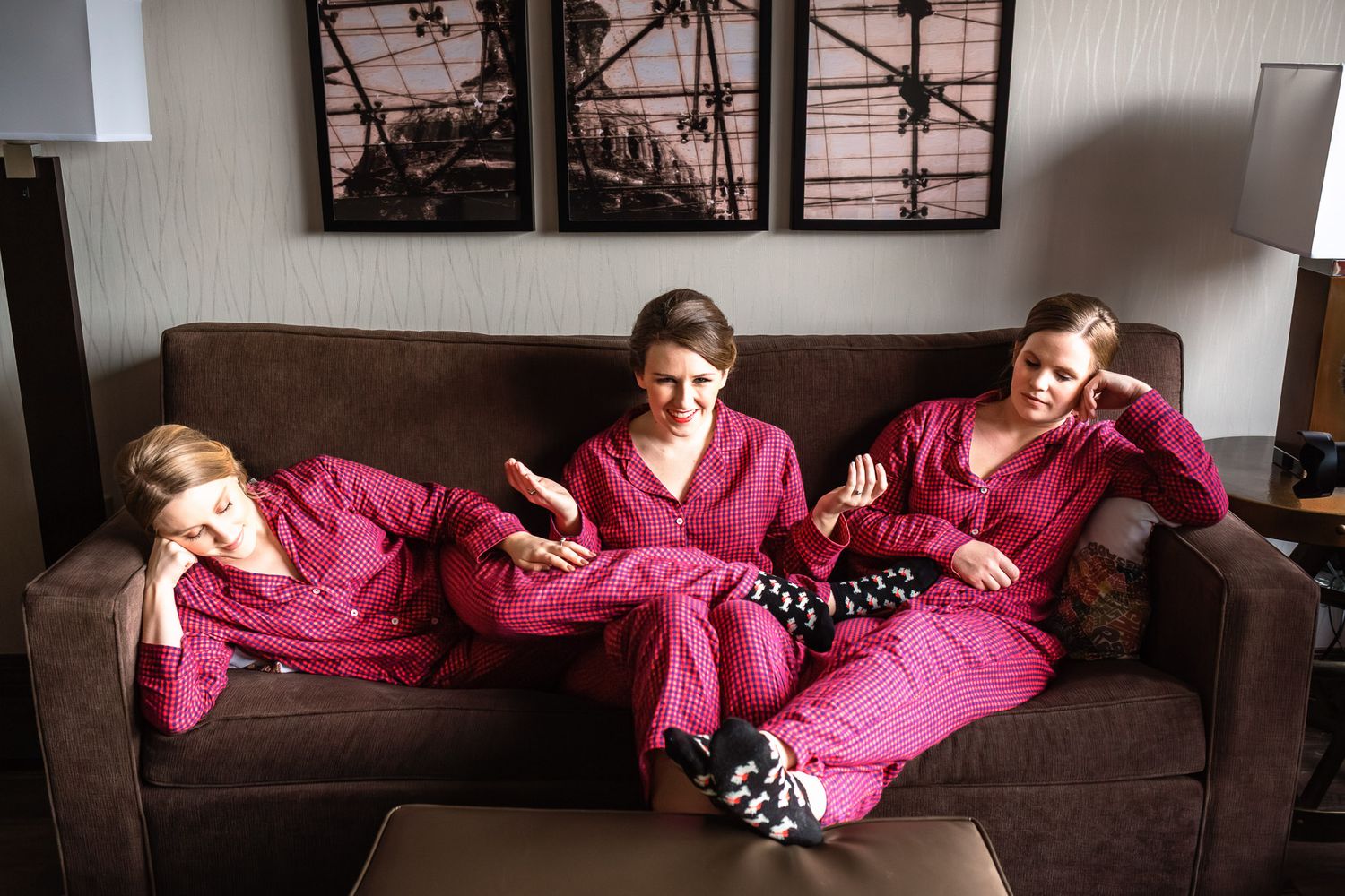 Three bridesmaids in matching pink pajamas relax casually on a brown sofa.