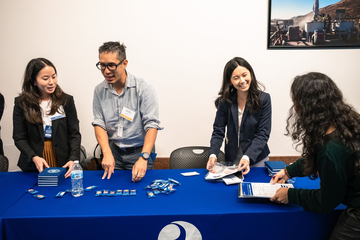 Three professionals in business casual attire engage with a visitor at a branded blue conference table.