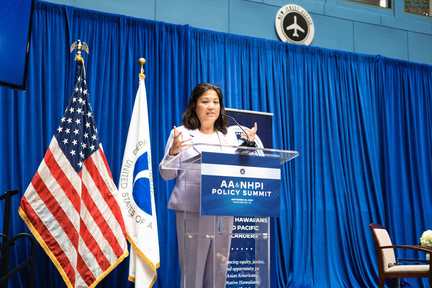 Woman speaks at podium during AA and NHPI Policy Summit with US flag and blue backdrop.