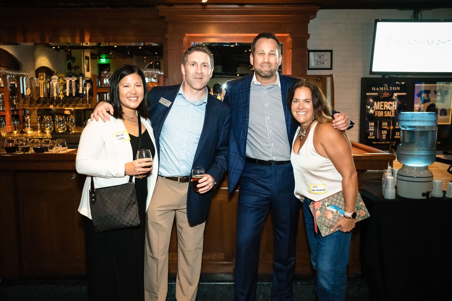 Four people smiling and posing together at a bar or restaurant social event.