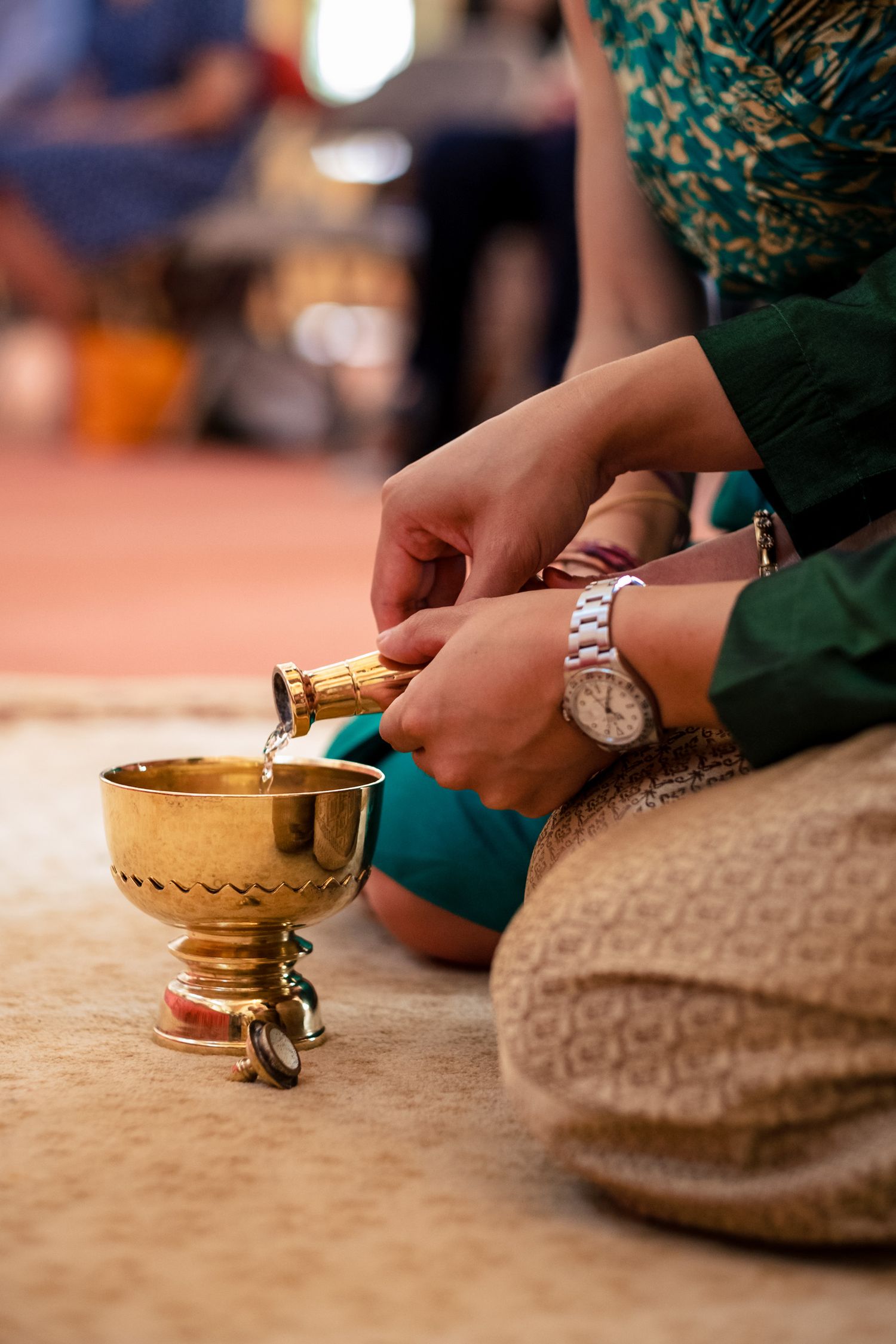Close-up of hands pouring water into a golden ceremonial bowl during a Thai Buddhist wedding ritual.