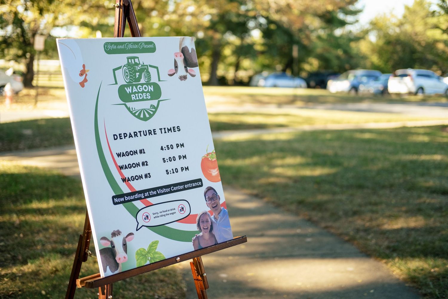 Wagon ride departure schedule sign on easel at outdoor wedding venue on sunny day.
