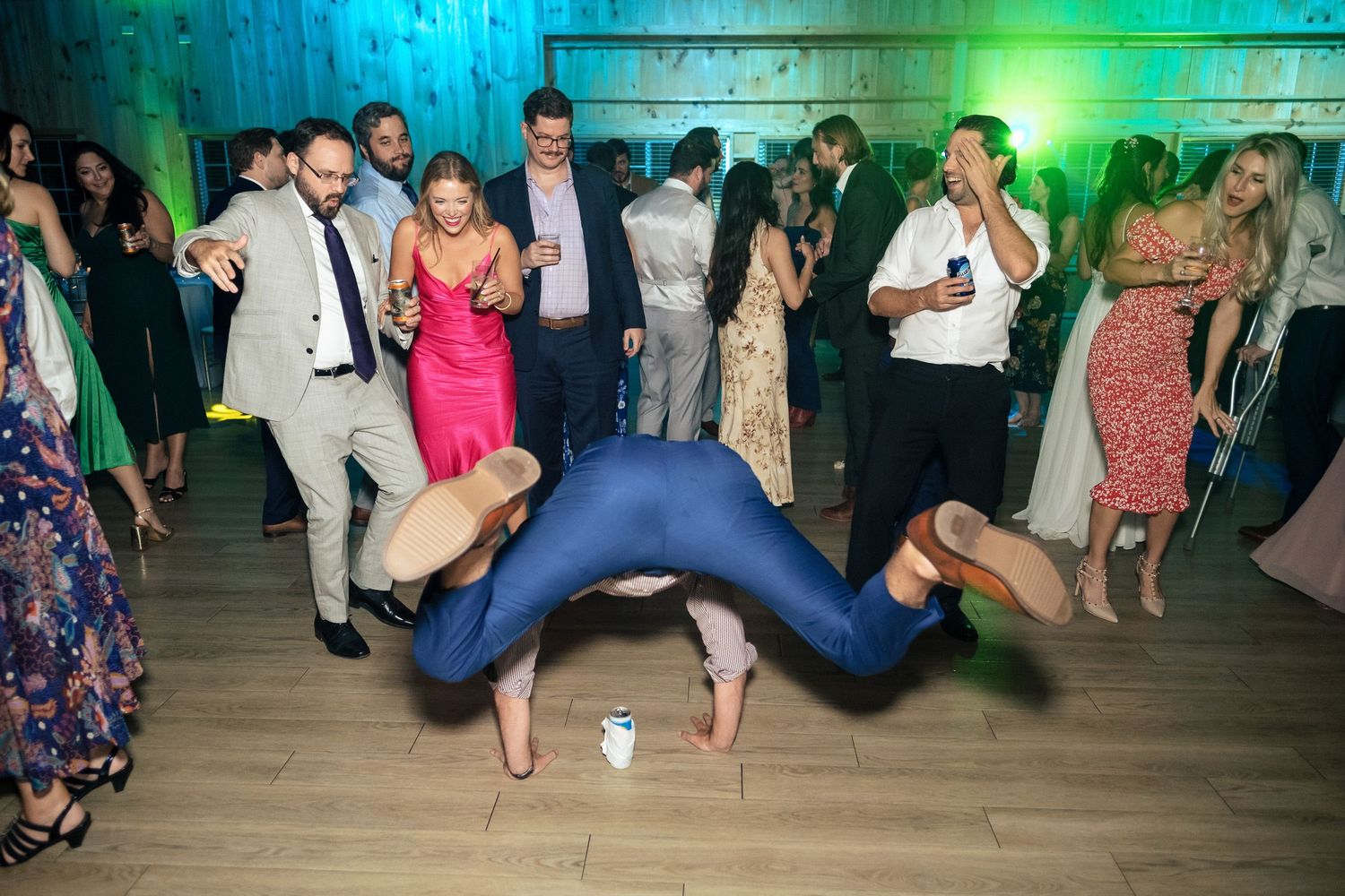 Wedding guest performing breakdance move on dance floor while guests cheer at lively reception.