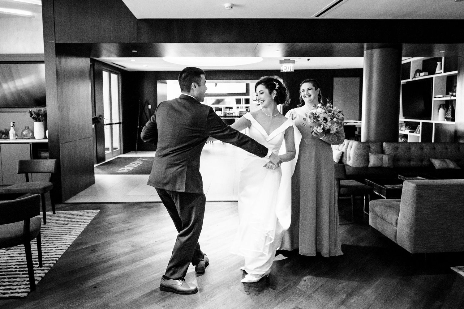 Bride and groom share a joyful first look moment in a modern hotel lobby in black and white photo.