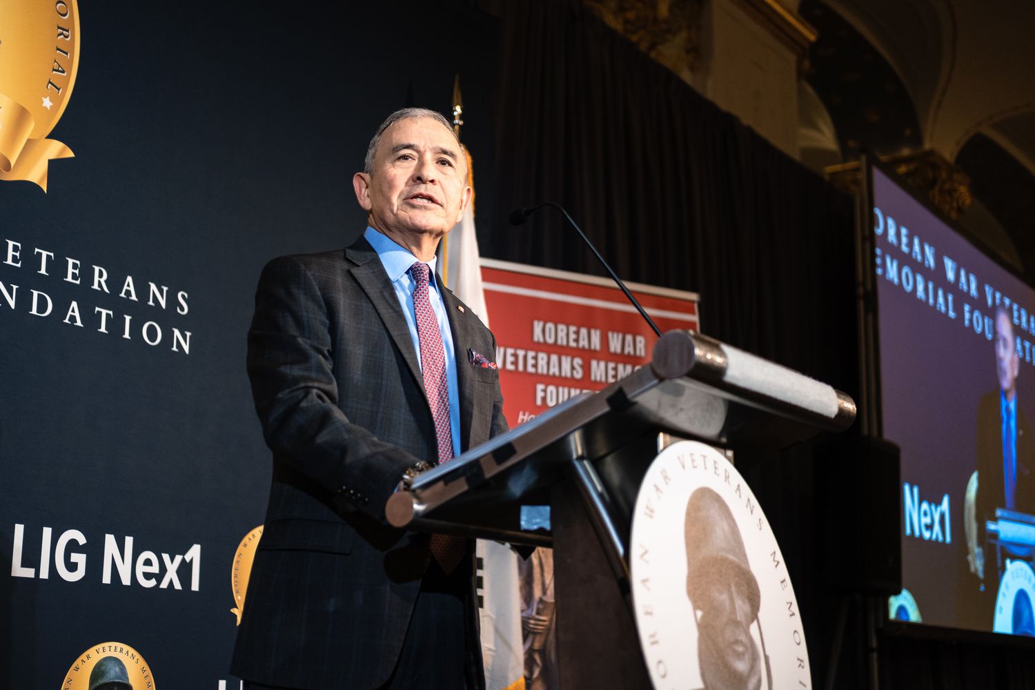 A man in a suit delivers a speech at a Korean War Veterans Memorial Foundation fundraising gala event.