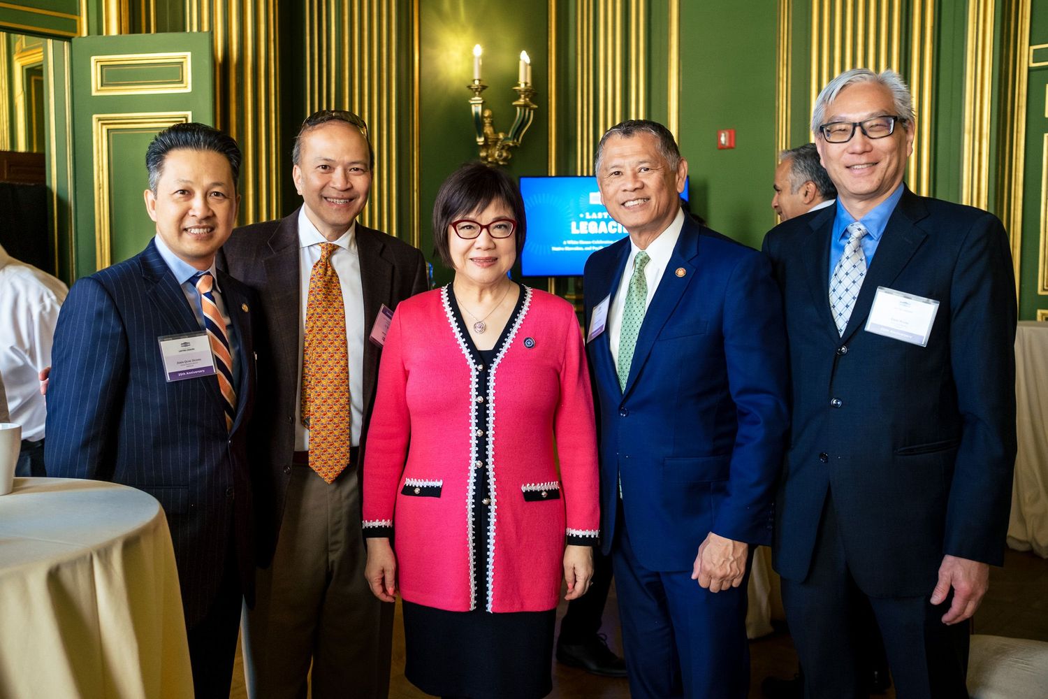 Five professionals pose together smiling at a formal networking event in an elegant green-walled venue.