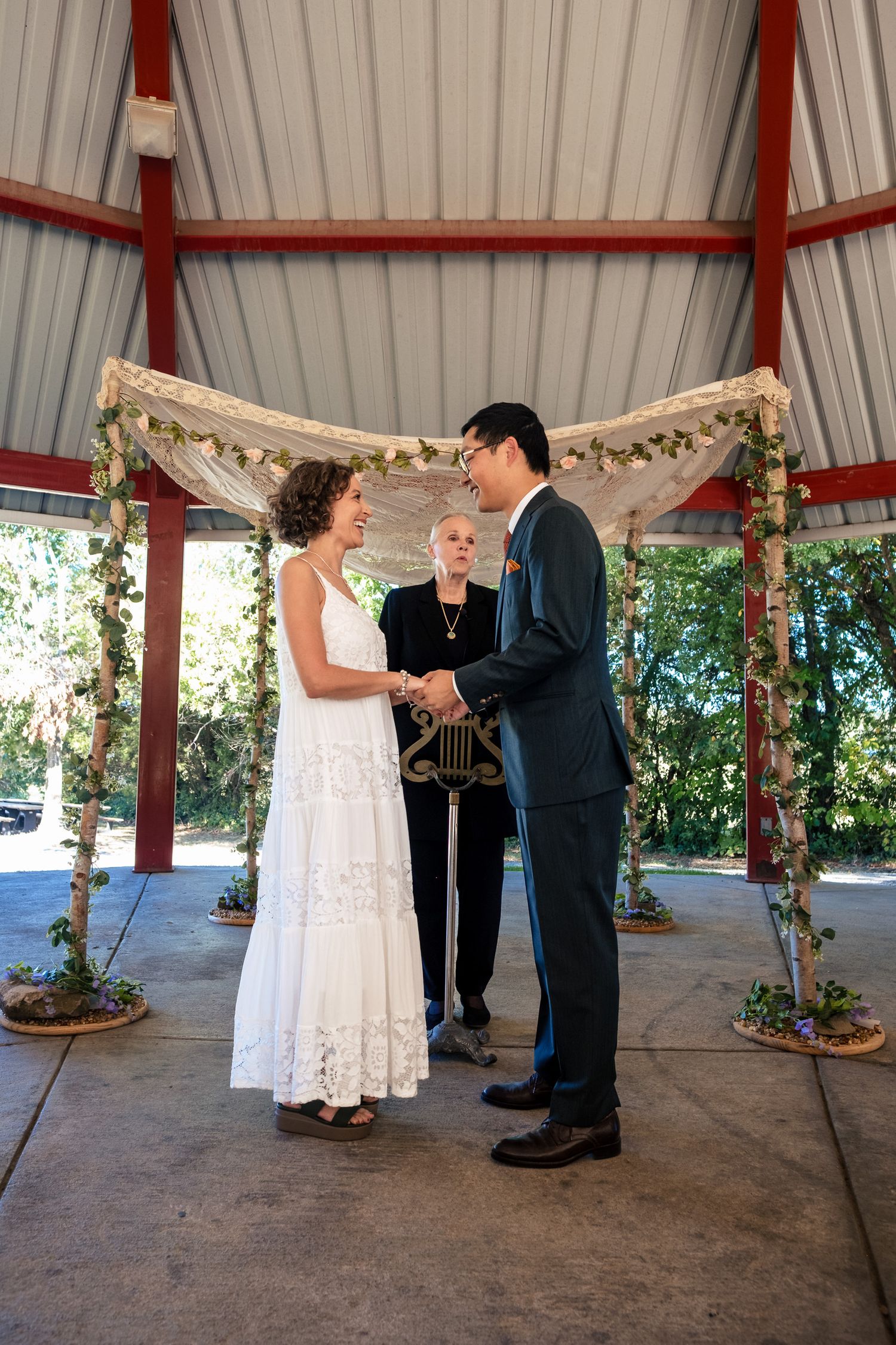 Bride and groom exchange vows under a floral arch at an outdoor wedding ceremony with officiant.