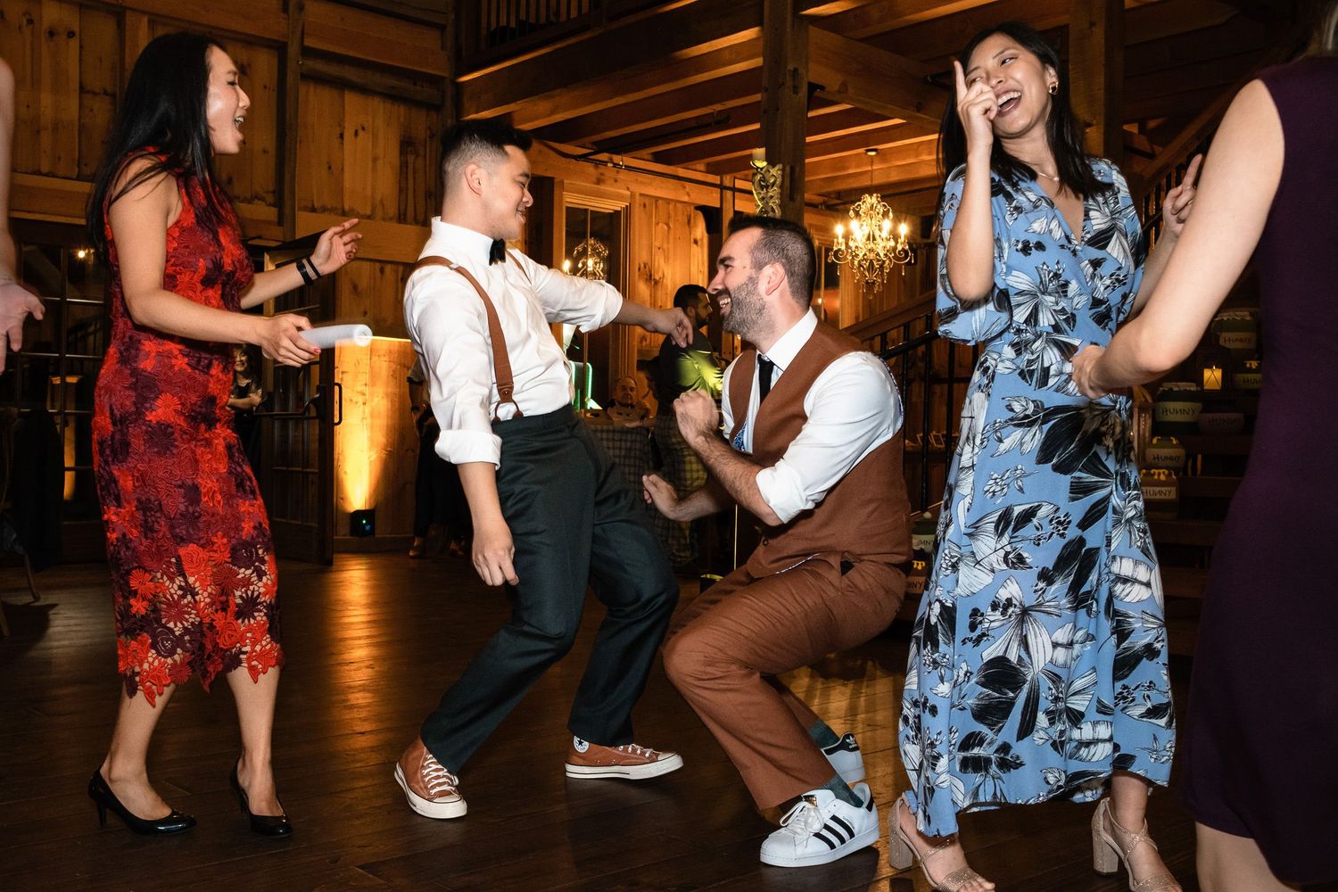 Wedding guests laugh and dance together in a rustic barn venue with warm lighting.