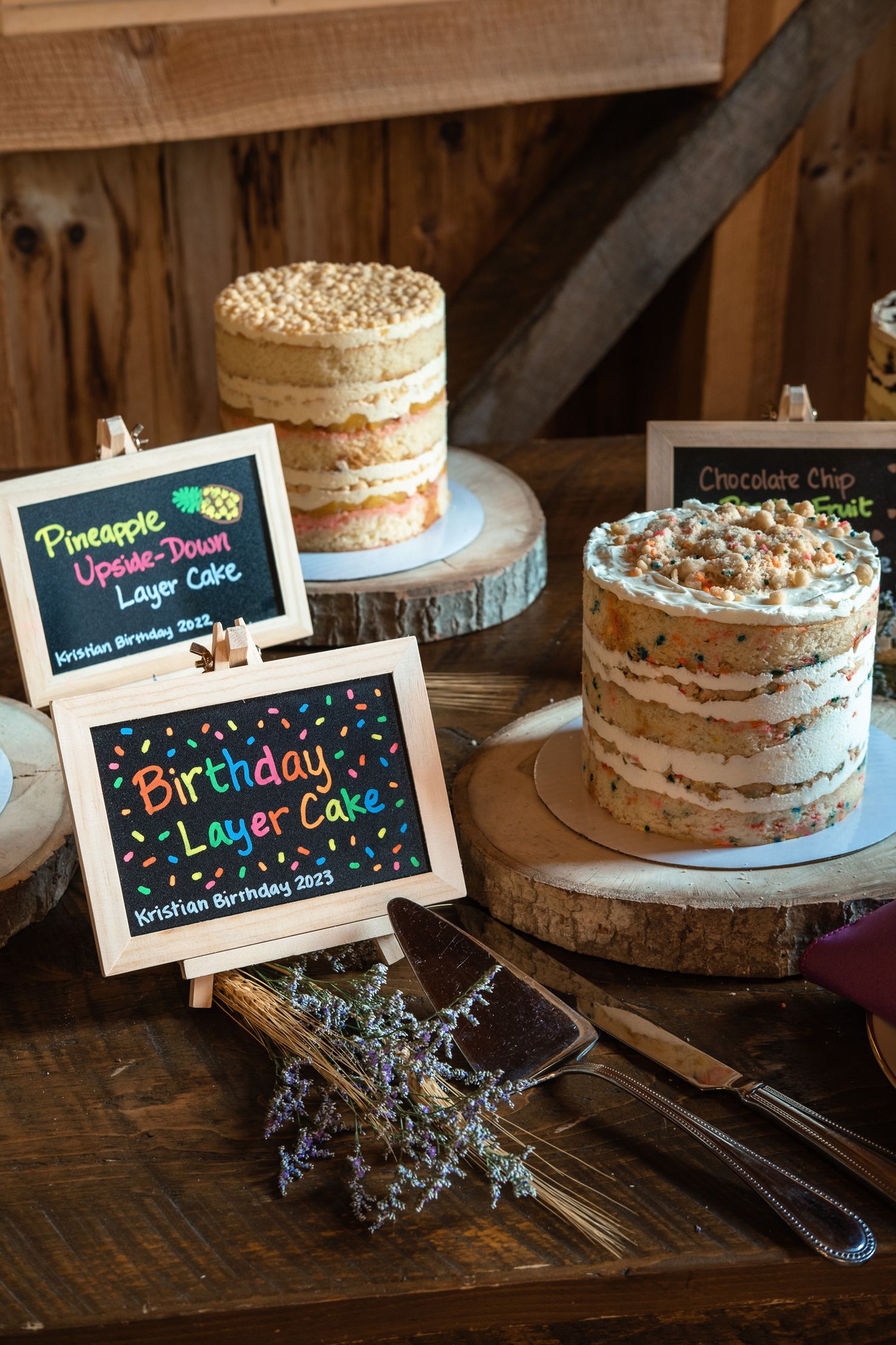 Rustic wedding dessert table featuring birthday layer cake and pineapple upside-down cake signs.