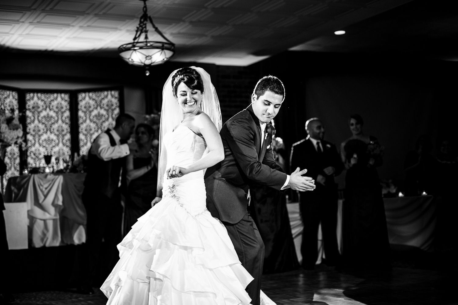 Bride in layered white gown and groom share their first dance at elegant wedding reception.