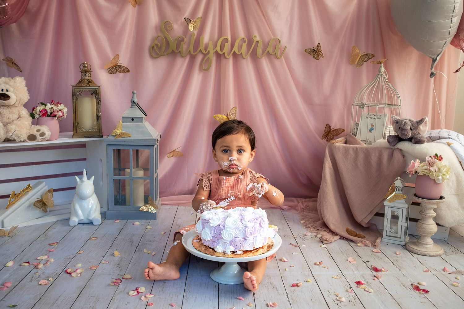 Baby girl in pink dress smashing first birthday cake during professional photo session.