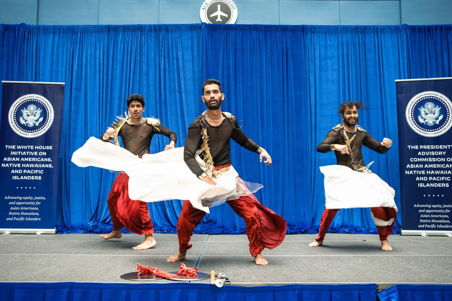 Three men perform an energetic traditional South Asian folk dance at a White House AAPI event.