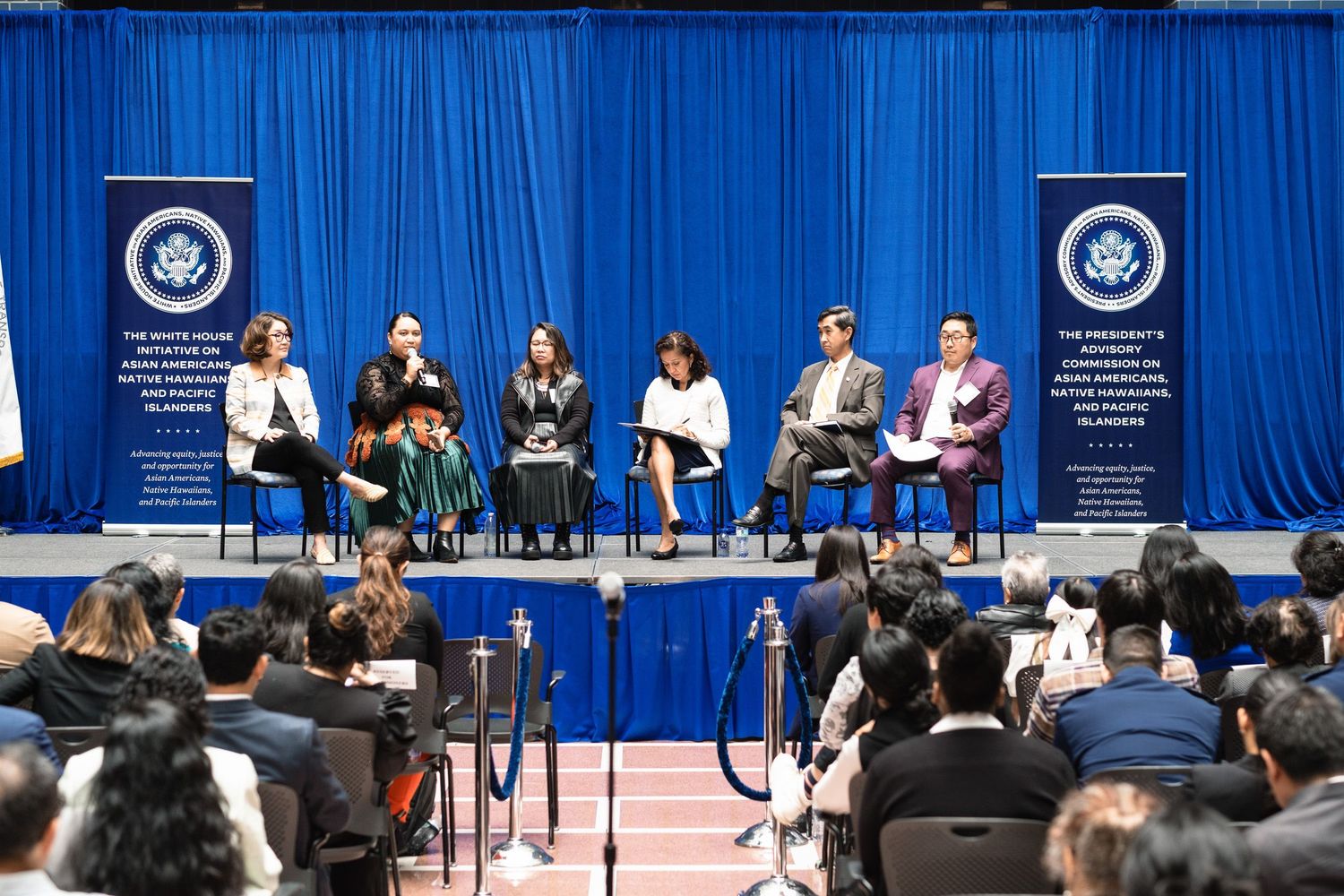 Panel discussion on stage at White House Initiative on Native Education conference with seven speakers seated before audience.