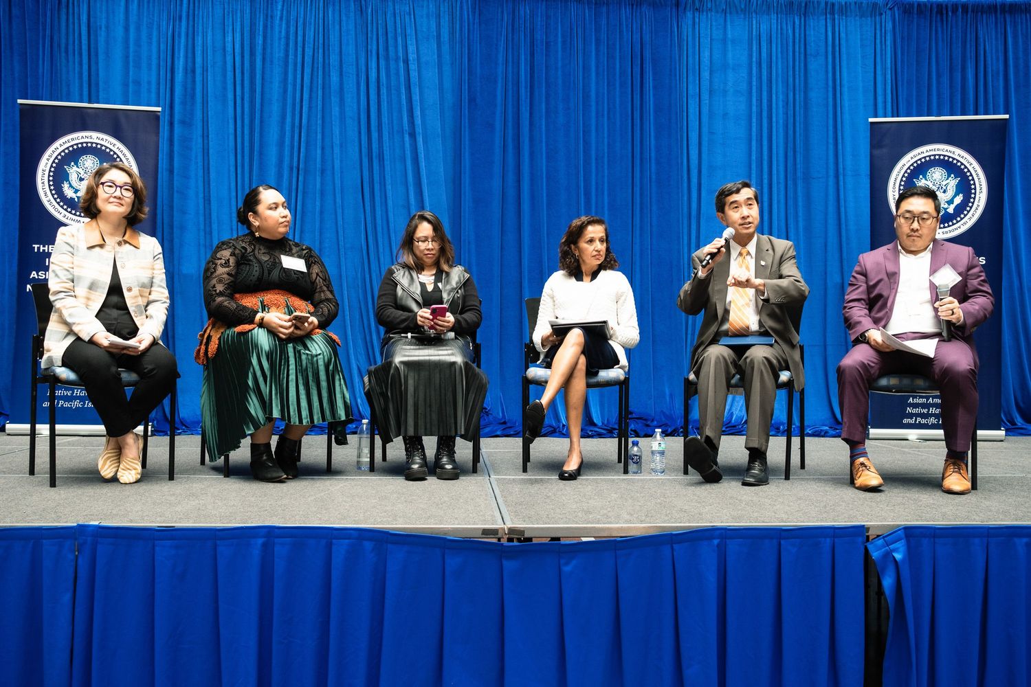 Panel of six diverse professionals seated on stage at a White House initiative conference event.