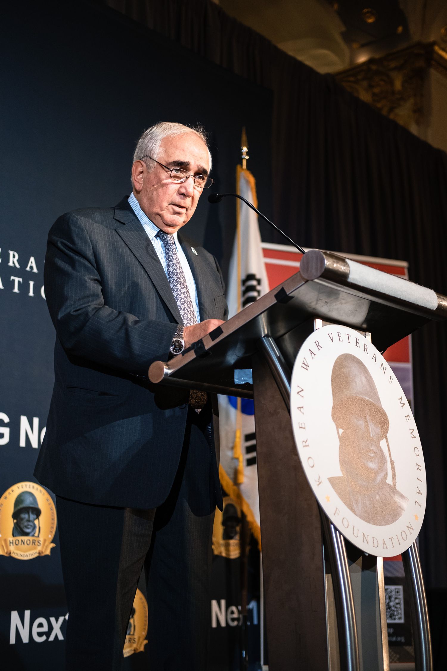 Senior speaker addresses audience at Korean War Veterans Memorial Foundation Honors podium during formal event.