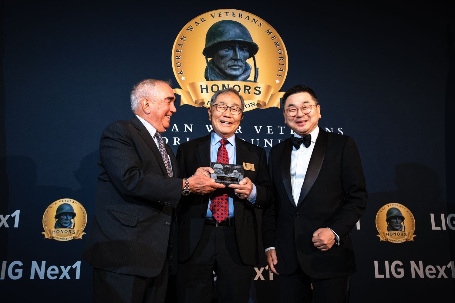 Two men present an award to a veteran at the Korean War Veterans dinner honors event with LIG Nex1.