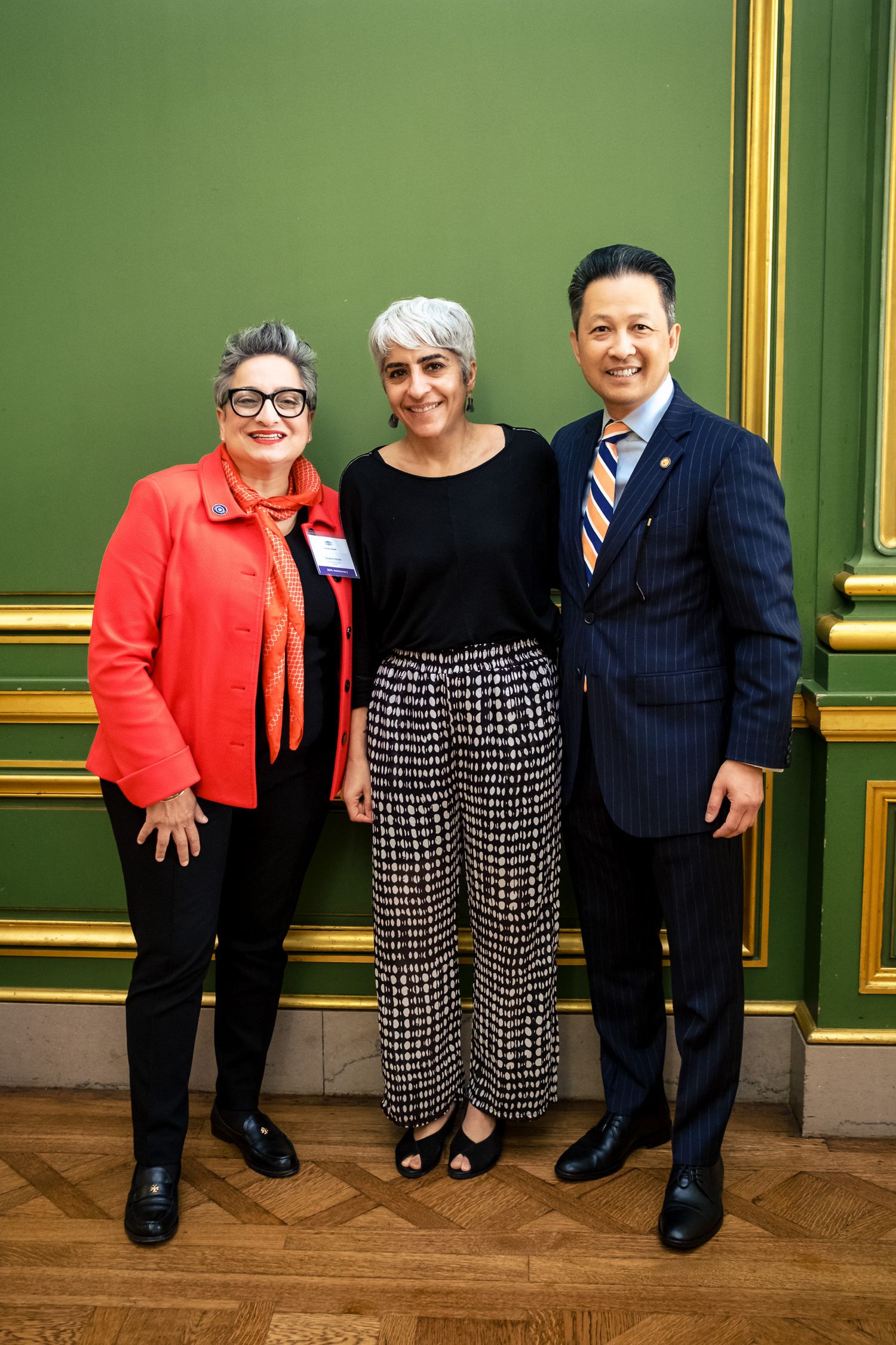 Three professionals posing together in front of a green wall at a formal event.