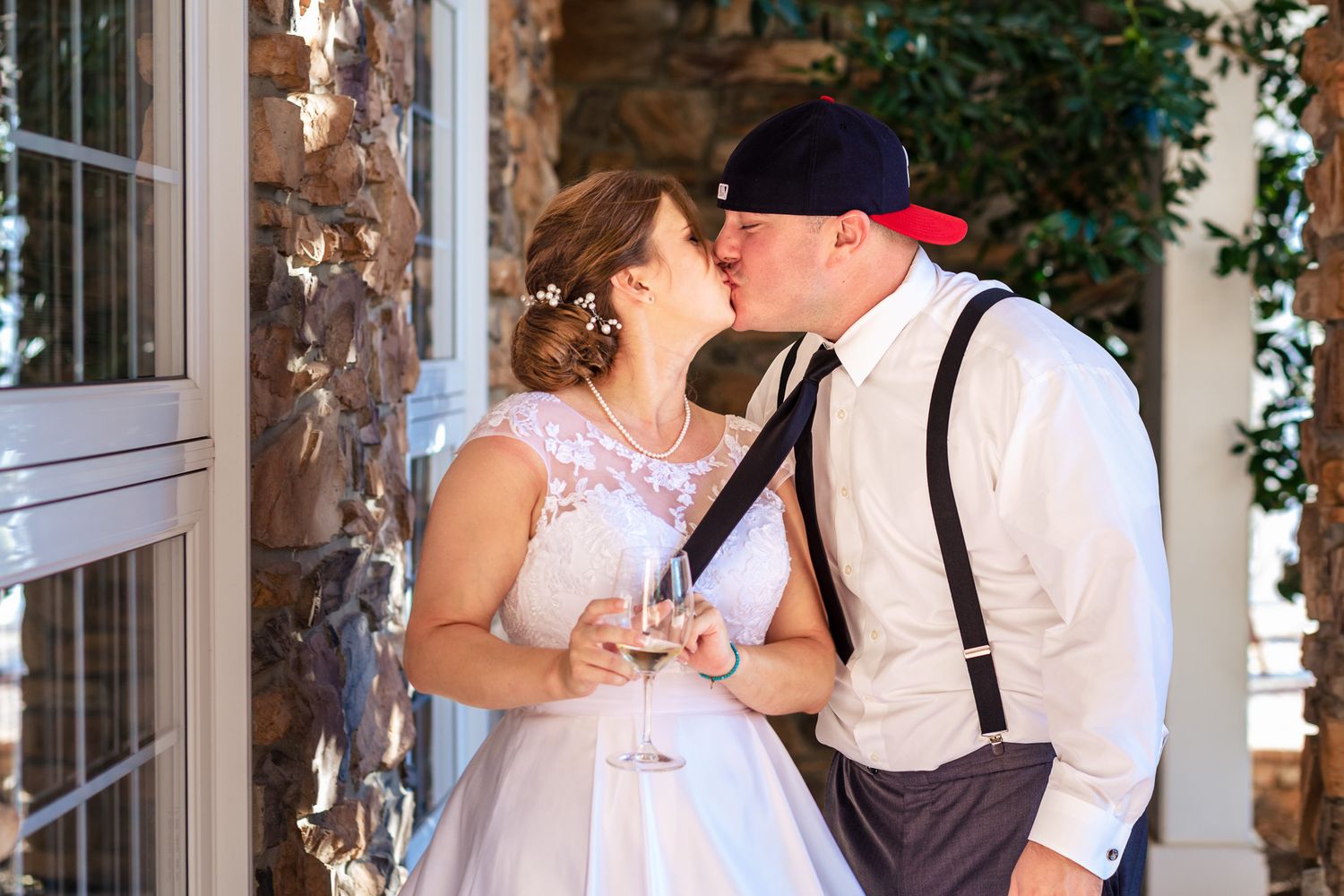 Bride and groom sharing a kiss while holding champagne glasses outside a stone building.