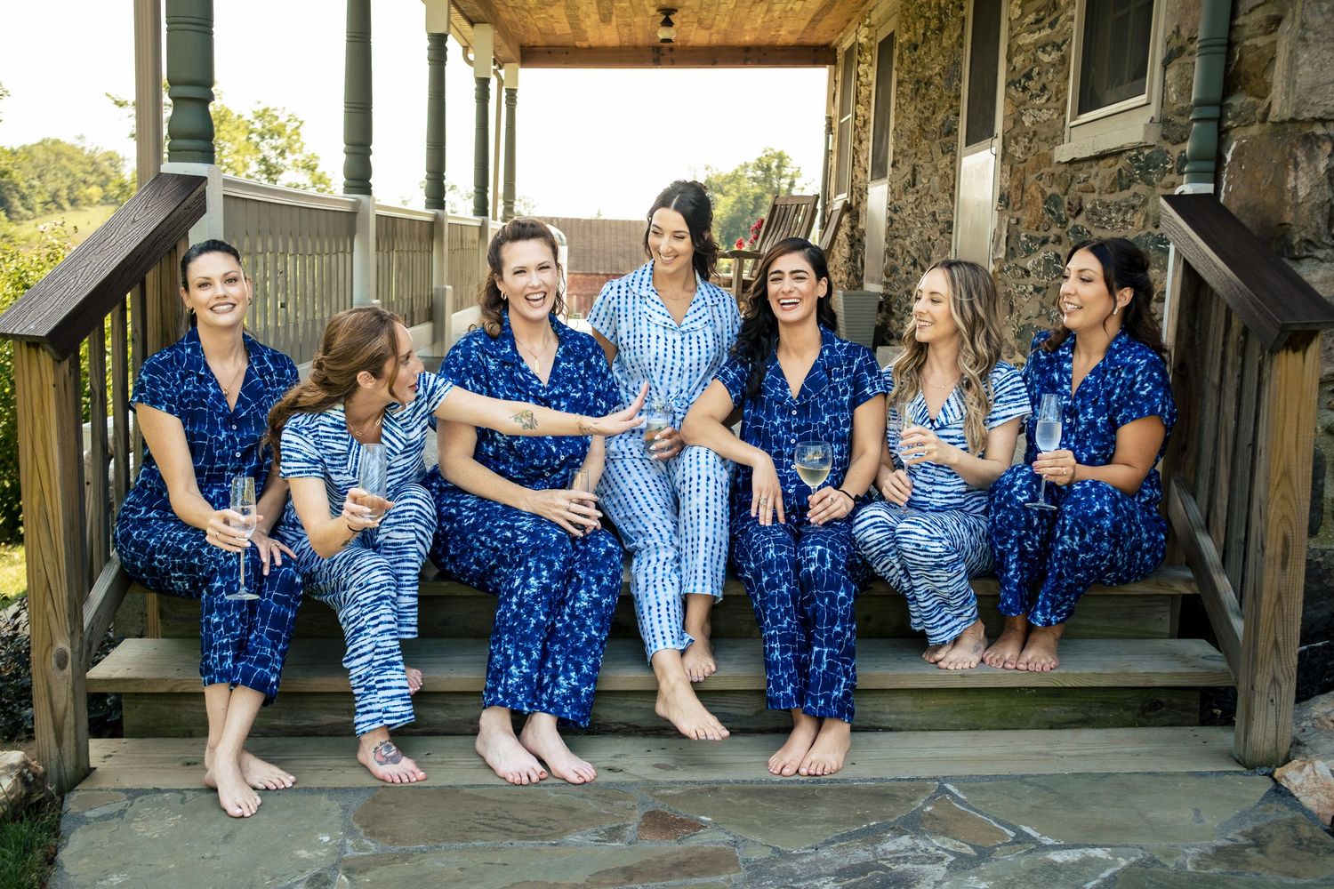 Bridesmaids in coordinating blue floral pajamas sitting and laughing on stone steps together.