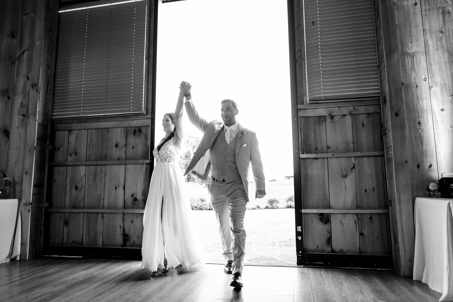 Bride and groom make a grand entrance through rustic barn doors in black and white wedding photo.