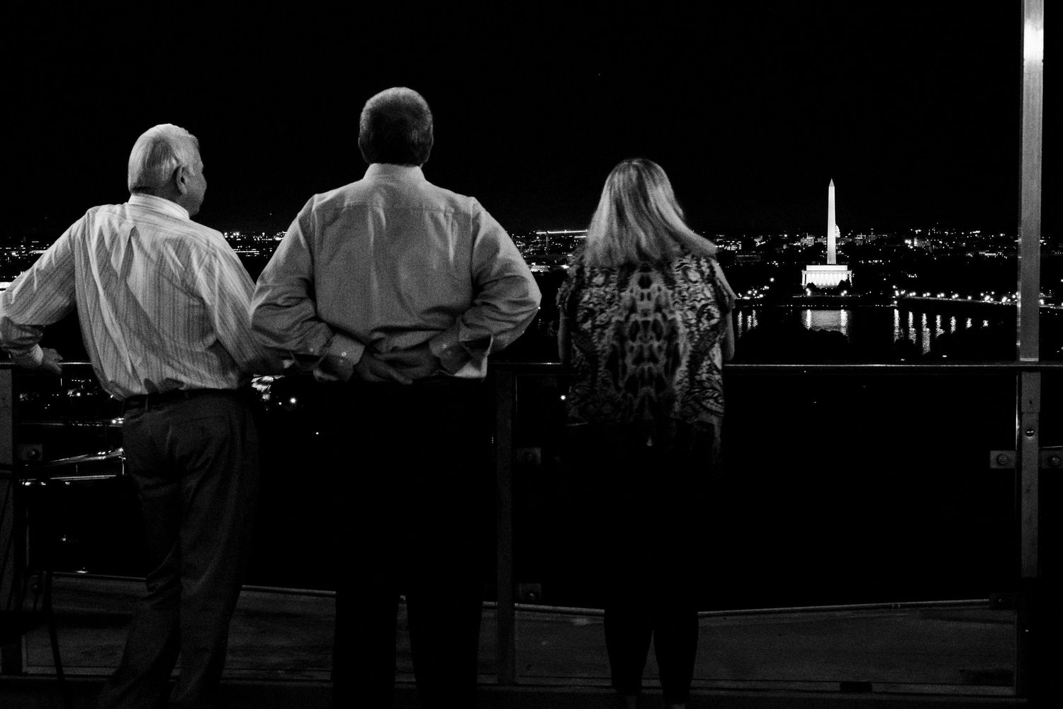 Three guests stand together in black and white photo admiring a city skyline at night.