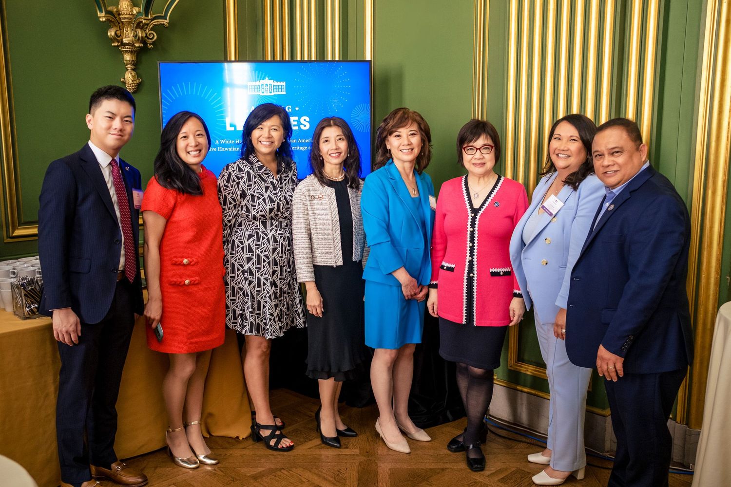 Group of eight Asian professionals posing together at a formal event in an elegant green-walled room.