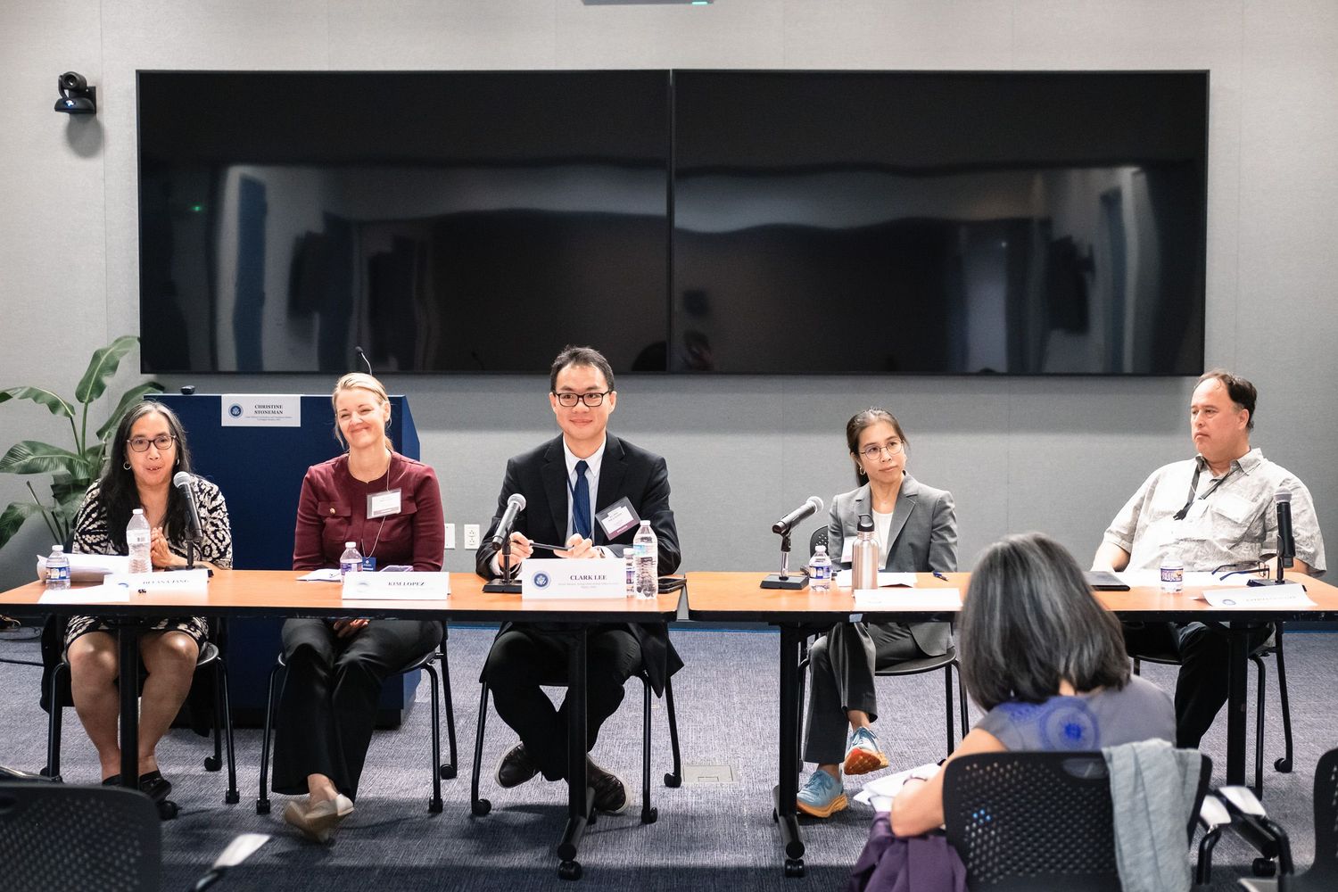Five panelists seated at a conference table during a professional panel discussion in a modern meeting room.