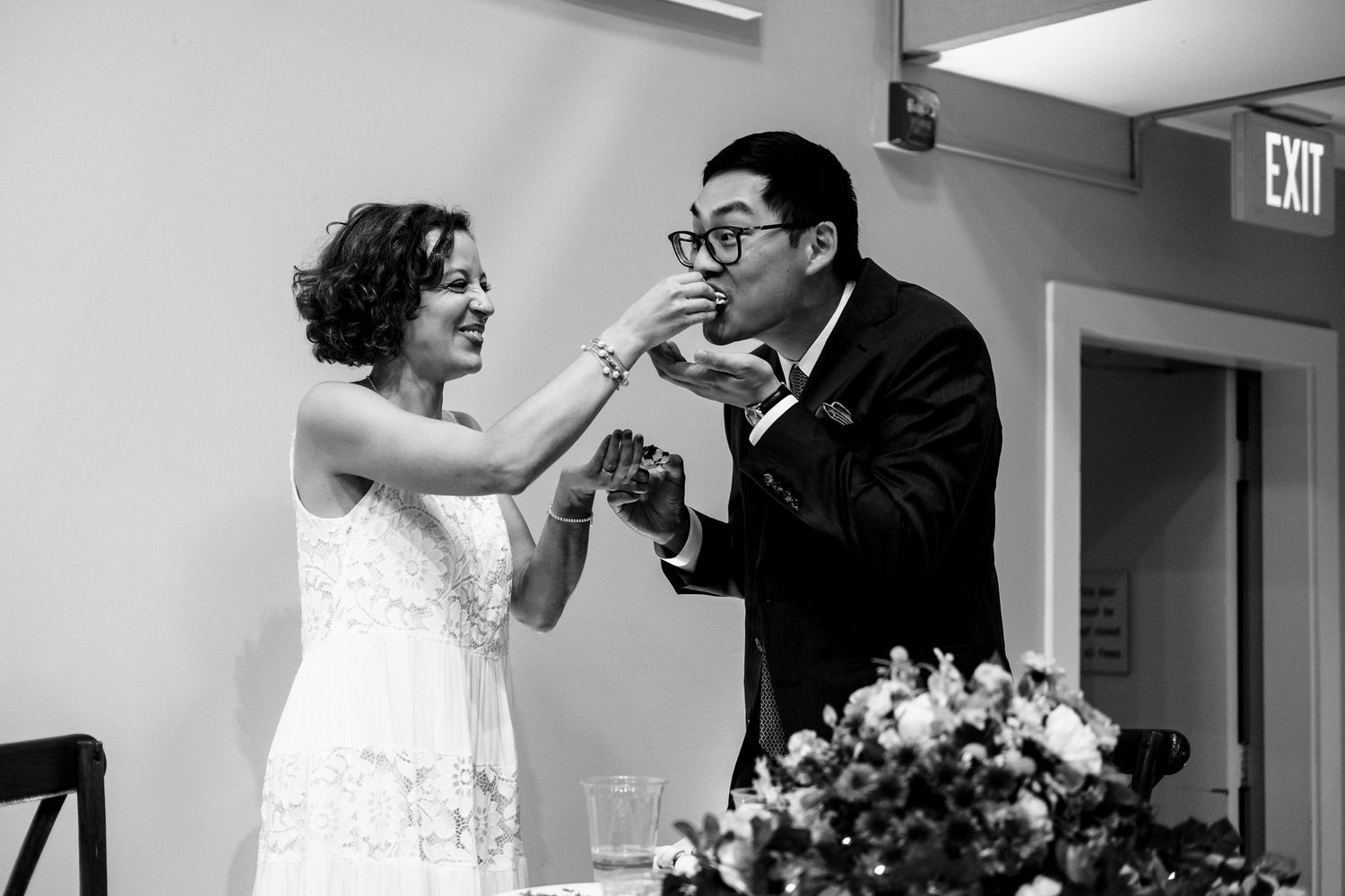 Bride and groom share a joyful cake tasting moment in black and white wedding portrait.